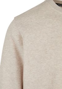 Gros plan d'un pull ras du cou beige montrant la texture et les détails de la couture de l'épaule sur le côté gauche.