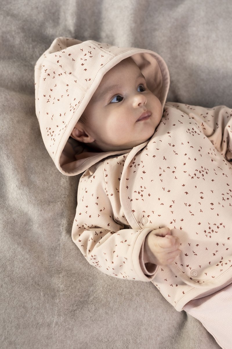 Helle rosa Babyjacke mit Kapuze, verziert mit kleinen roten Blumenmustern, aus weichem Baumwollmaterial und mit Druckknopfverschluss. Heller, texturierter Hintergrund.