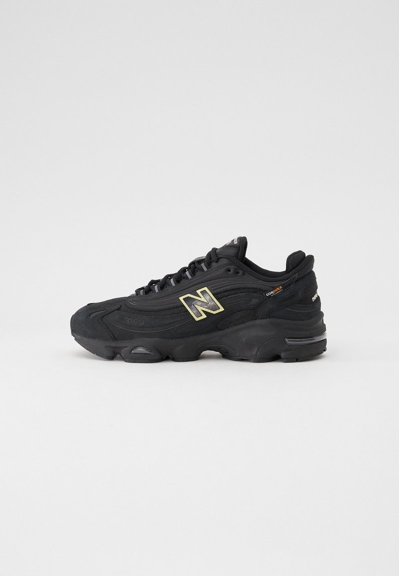 Baskets noires New Balance avec logo doré, semelle épaisse et amorti visible, vues de côté sur fond blanc uni.