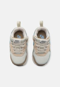 Sneakers Nike z beżową siateczką na górze, z niebieskimi akcentami, jasnobrązowymi detalami i szarymi sznurówkami. Zawierają pętelkę na pięcie ułatwiającą zakładanie.