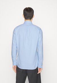 Lichtblauwe langemouwen shirt gezien van achteren, met een rechte snit, knoopmanchetten en een rugplooi detail.
