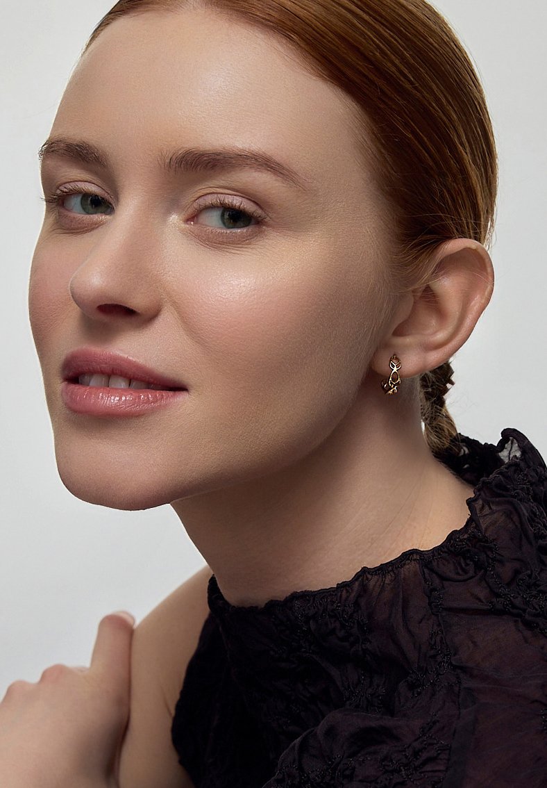 Złote kolczyki w kształcie kropli z misternym wzornictwem, z delikatnymi akcentami. Tło jest neutralne, co podkreśla biżuterię.