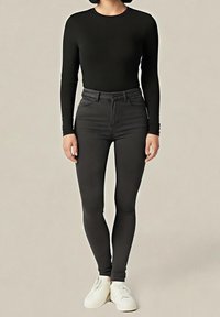 Czarna bluzka z długim rękawem w połączeniu z czarnymi, przylegającymi dżinsami z wysokim stanem oraz białymi trampkami. Gładka faktura bez widocznych wzorów ani zdobień.