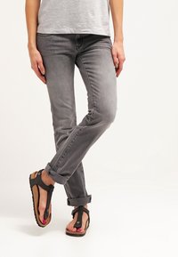 Jeans in denim grigio con orli arrotolati, abbinati a sandali infradito neri con una base dalla superficie texturizzata.