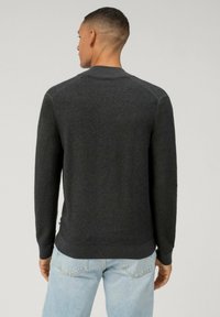 Donkergrijze geribde trui met een ronde halslijn en lange mouwen. Heeft een aansluitende zoom, textuurstof en een labeldetail aan de zijkant.