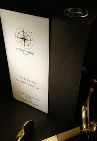 Witte rechthoekige verpakking met zwarte tekst, met een kompaslogo; geplaatst naast een gouden accent, op een donkere achtergrond.