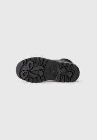 Semelle de chaussure en caoutchouc noir avec un relief texturé, ornée de motifs en forme de cœur et de nœud. Bords renforcés pour plus de durabilité.