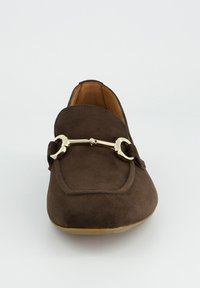 Brauner Wildleder-Slipper mit goldfarbenem Metall-Horsebit-Detail oben, flacher Sohle und hellbraunem Innenfutter, von vorne gezeigt.