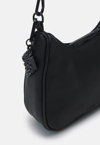 Sac à main noir texturé de forme circulaire, doté d'une fermeture éclair et d'une étiquette de marque décorative attachée à une bandoulière en chaîne.