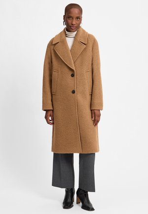 Brown wool coat featuring a wide lapel, two front pockets, and three large black buttons. Paired with gray wide-leg trousers and black heels.