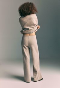 Bežový sveter a zodpovedajúce široké nohavice z mäkkej pleteniny. Oblečenie má voľný strih s mierne skráteným dizajnom.