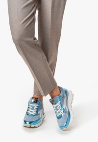 Jasnoniebieskie buty sportowe z siateczką i błyszczącymi akcentami, z białymi sznurowadłami i teksturowaną podeszwą, w zestawieniu z beżowymi spodniami eleganckimi.