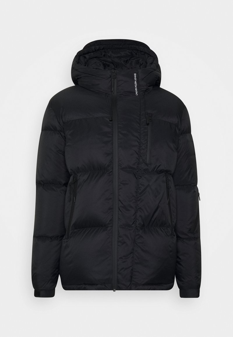 Veste matelassée noire avec capuche, dotée d'une fermeture éclair frontale, de deux poches latérales et de détails de marque sur l'épaule. Tissu lisse et léger.