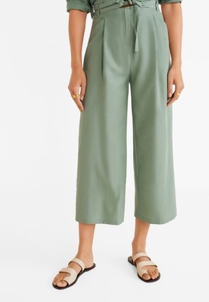 Woman wearing high-waist, wide-leg sage green cropped pants with a fabric belt, paired with beige double-strap flat sandals.