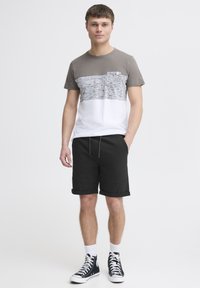 T-shirt gris et blanc avec un panneau texturé horizontal, associé à un short noir et des baskets montantes noires. Design simple, coupe décontractée.