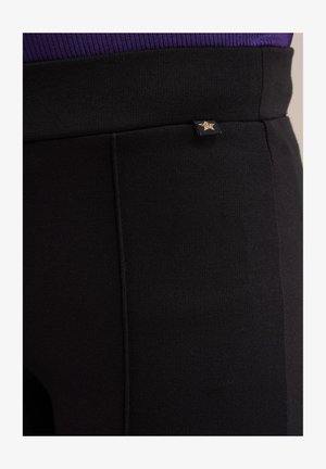 Leggings atletice negre, fabricate dintr-un material texturat, având un mic accent cu stea aurie și detalii cu cusături vizibile de-a lungul picioarelor.