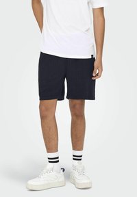 Pantalones cortos azul marino con una tela texturizada, de longitud por encima de la rodilla y con bolsillos laterales, combinados con zapatillas blancas y calcetines de rayas.49