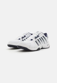 Baskets blanches avec des accents bleu marine, dotées d'une tige en cuir lisse, d'une semelle texturée et de plusieurs rayures le long du côté pour le soutien.