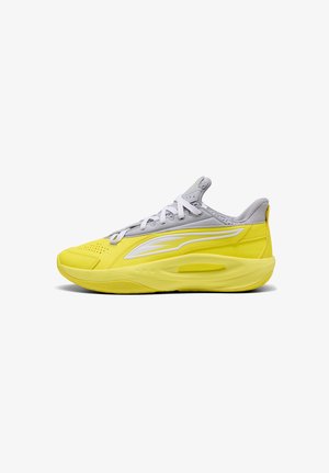 Lavtskåret atletiksneaker med gul sål og side, grå overdel, hvide snørebånd og hvidt logo på siden.