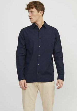 Camicia a maniche lunghe blu navy con colletto a punta e bottoni in ottone, realizzata in un tessuto di cotone leggero e liscio.