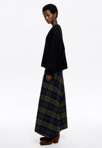 Czarny oversize sweter z długim rękawem, zestawiony z maxi spódnicą w zielono-niebieską kratę. Brązowe zamszowe botki za kostkę dopełniają outfit.