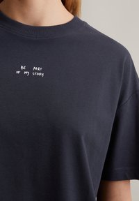 T-shirt en coton navy avec un col rond ; présente un texte imprimé blanc "FAIS PARTIE DE MON HISTOIRE" sur la poitrine dans une police décontractée.