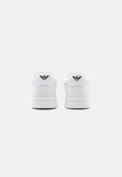 Paire de baskets blanches Emporio Armani vues de dos, montrant un logo noir sur la languette du talon et le nom de la marque embossé sur la semelle.