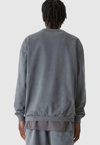 Szürke pamutháló, laza szabással, bordás mandzsettákkal és szegéllyel, valamint puha tapintással. Kerek nyakú és esőhüvelyes vállakat tartalmaz.