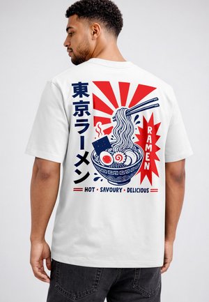 Mann trägt weißes T-Shirt mit rot-blauer Grafik einer dampfenden Ramen-Schüssel, Essstäbchen, japanischem Text und den Worten heiß, herzhaft, lecker.
