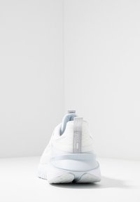 Białe buty sportowe z siateczkową cholewką, szarymi akcentami, zaokrąglonym obcasem oraz pętelką z tyłu. Teksturowana podeszwa dla lepszej przyczepności.