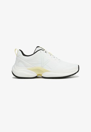 White athletic shoes with a textured upper, yellow accents on the sides, and a black outsole. Features padded collar and laces.