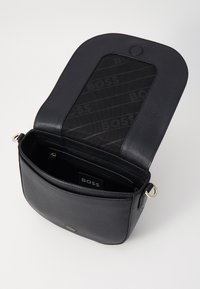 Borsa a tracolla in pelle nera con finitura liscia, forma curva, chiusura magnetica e interno decorato con il logo "BOSS."