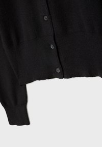 Section d'un cardigan noir en maille montrant trois boutons et un poignet côtelé sur une manche longue, sur un fond clair.