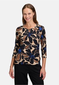 Beżowa bluzka z długim rękawem w kwiaty, z dużymi czarnymi i brązowymi kwiatami z niebieskimi akcentami, okrągłym dekoltem oraz miękkim, elastycznym materiałem.