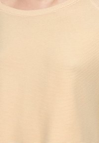 Φωτεινό μπεζ ριμπ πλεκτό πουλόβερ με στρογγυλή λαιμόκοψη και απαλή υφή. Το ύφασμα έχει στενή, ομοιόμορφη ύφανση σε όλο το μήκος.