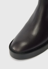 Fekete bőr bokacsizma lekerekített orral, sima textúrával és vastag fekete talppal. A dizájn elegáns és minimalista.