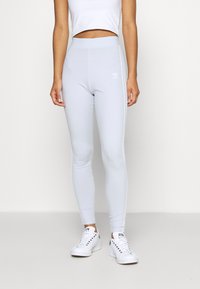 Helle graue Leggings in einer körperbetonten Passform mit einem elastischen Bund, die weiße Seitenstreifen und ein kleines Markenlogo auf der Vorderseite aufweisen.