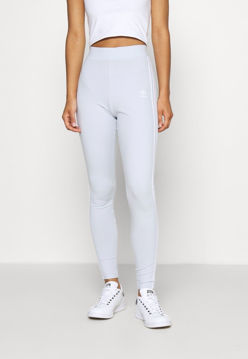 Helle graue Leggings in einer körperbetonten Passform mit einem elastischen Bund, die weiße Seitenstreifen und ein kleines Markenlogo auf der Vorderseite aufweisen.