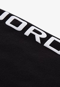Tissu noir à la texture douce avec de grandes lettres blanches en relief épelant "JORDAN" sur toute la surface.