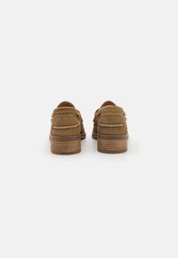 Chaussures en suède marron avec un petit talon. Dotées de coutures lisses, d'une fermeture à double bride et d'une semelle en bois texturée.