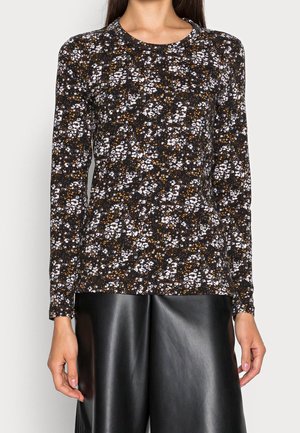 Vrouw draagt een zwart langarmig shirt met een kleine witte en oranje bloemenprint, gecombineerd met losse zwarte leren broek.