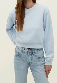 Sudadera corta de color azul claro con cuello redondo acanalado y mangas largas, combinada con jeans de tiro alto azul claro. Tejido texturizado, ajuste casual.