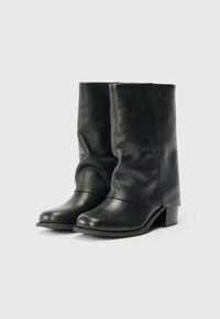 Botas de cuero negras a medio pantorrilla con tacones bajos y punteras redondeadas, de pie una al lado de la otra sobre un fondo blanco.