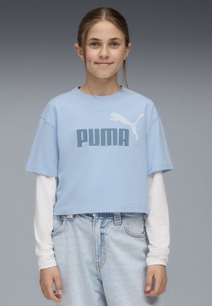 Jasnoniebieska krótka koszulka z dużą szaro-niebieską grafiką i logo "PUMA". Koszulka ma luźny krój i krótkie rękawy, noszona na białej koszulce z długim rękawem.