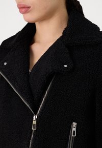 Zwarte schapenvacht jack met een brede kraag, zilveren hardware ritsen en zijzakken. Zachte textuur met een luxe uitstraling en gedetailleerde stiksels.
