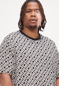 Svart og hvit T-skjorte med kort erme, med et geometrisk mønster og rund hals med solid svart kant. Lite logoakcent på forsiden.