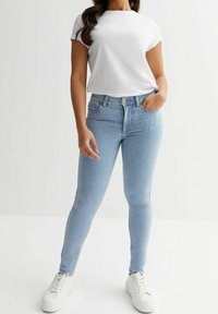 Vaqueros skinny de denim azul claro con cintura alta y diseño de cinco bolsillos, combinados con una camiseta blanca de manga corta y zapatillas blancas.