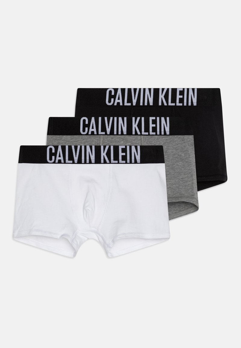 Drie paren herenboxershorts in wit, grijs en zwart. Elk heeft een elastische tailleband met "CALVIN KLEIN" in dikke letters erop gedrukt.