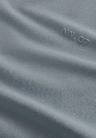Tessuto grigio chiaro con una sottile texture diagonale, con il testo in rilievo "NN. 07" vicino all'angolo in alto a destra.