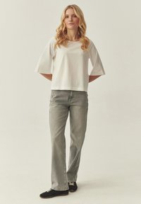 T-shirt en coton blanc à manches larges, associé à un jean en denim gris clair. La tenue est complétée par des baskets noires avec des lacets blancs.